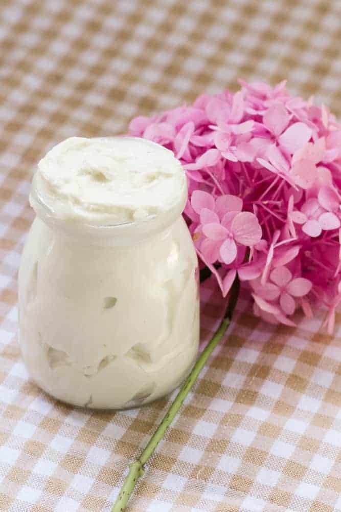 Tallow body butter in glass jar next to pink flowers.