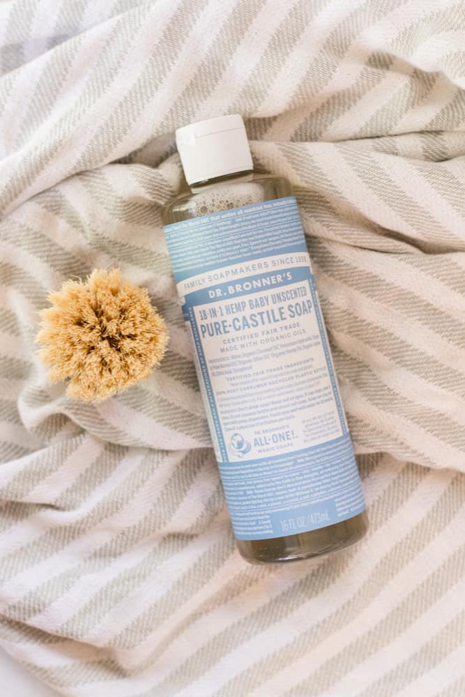 Unscented Castile Soap on white and gray towel with a wood scrub brush next to it.