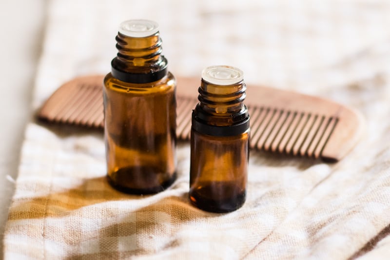 Hair growth essential oil bottles with wooden comb in background.
