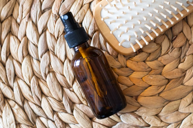 Essential oils for hair growth in a glass spray bottle on wicker mat.