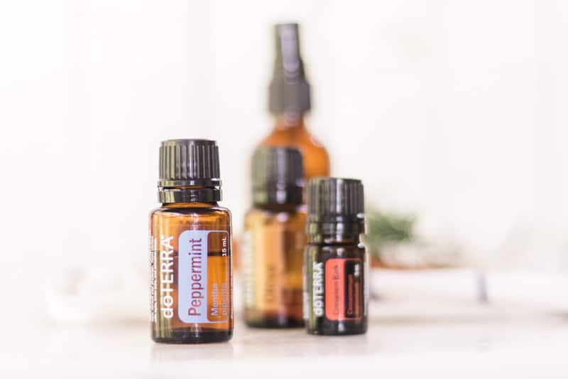 Peppermint, cinnamon, and clove essential oil sitting in front of homemade mouth rinse.