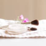 Homemade setting powder in a shallow dish with an applicator brush next to it.