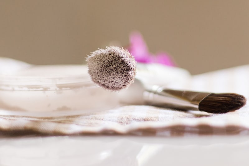 Makeup brush with a dab of setting powder on the end laying across a glass container.