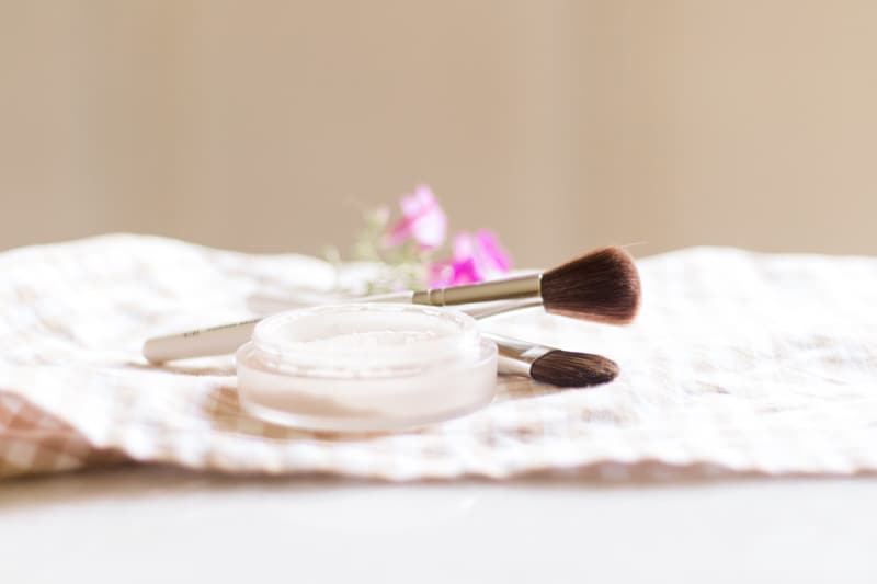 Homemade setting powder in a shallow dish with an applicator brush next to it.