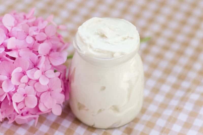 A small jar of tallow butter with pink flowers next to it on a checked table cloth. 