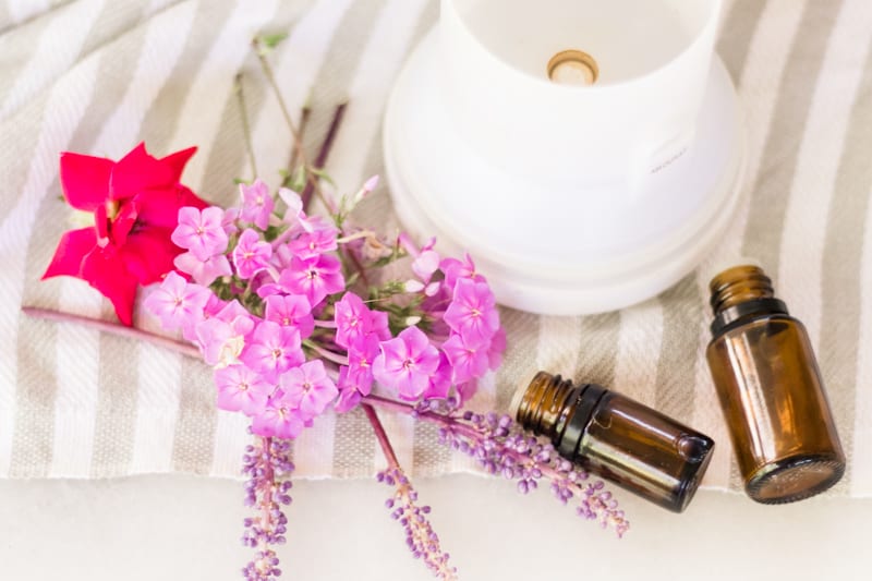 Essential oil diffuser, amber colored essential oil bottles, and flowers on white and gray striped towel.