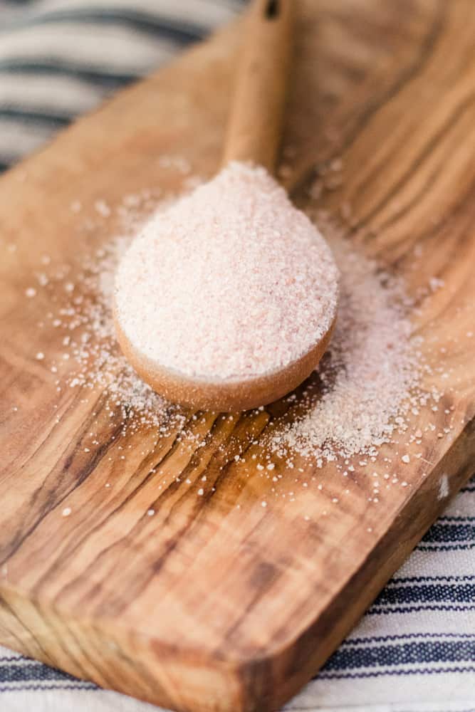 Pink Himalayan salt spilling out of wooden measuring spoon. 