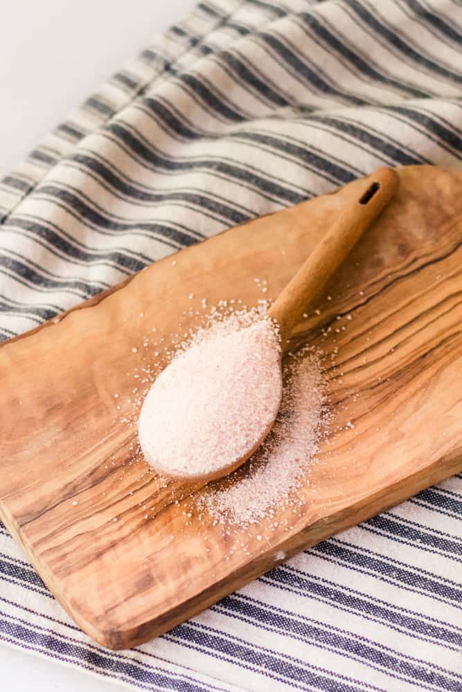 Pink Himalayan salt in wooden tablespoon on cutting board.