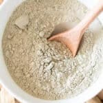 Bentonite clay powder in glass bowl being stirred with a wooden spoon.