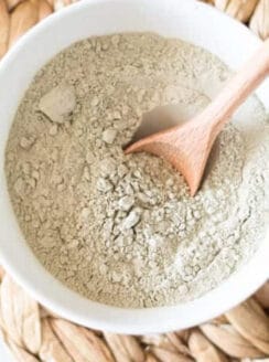 Bentonite clay powder in glass bowl being stirred with a wooden spoon.