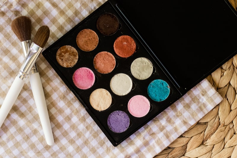 Eyeshadow on white and tan checker towel with white brushes by it.