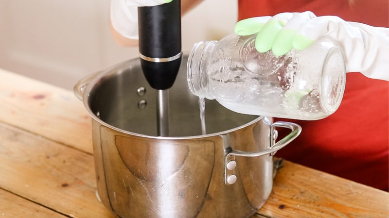 Adding lye water to saucepan of oils, mixing with an immersion blender.