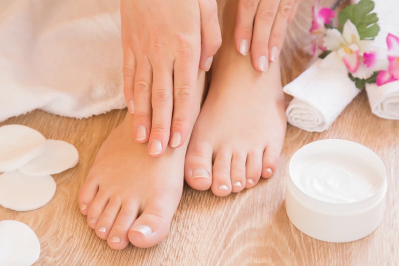 Women feet and hands with lotion and flowers by them. 