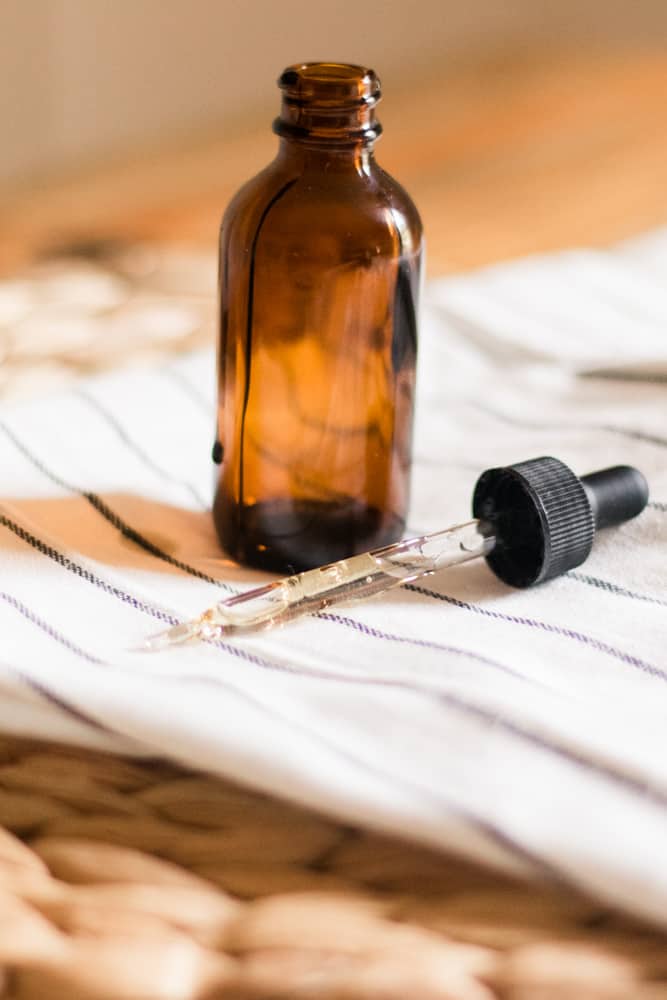 Black castor oil serum in amber glass jar with dropper sitting next to it.