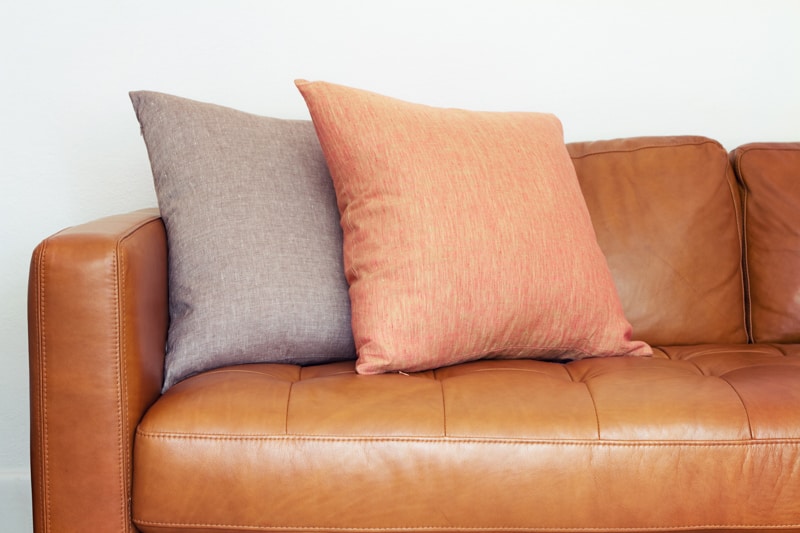Leather couch with two throw pillows sitting on it.
