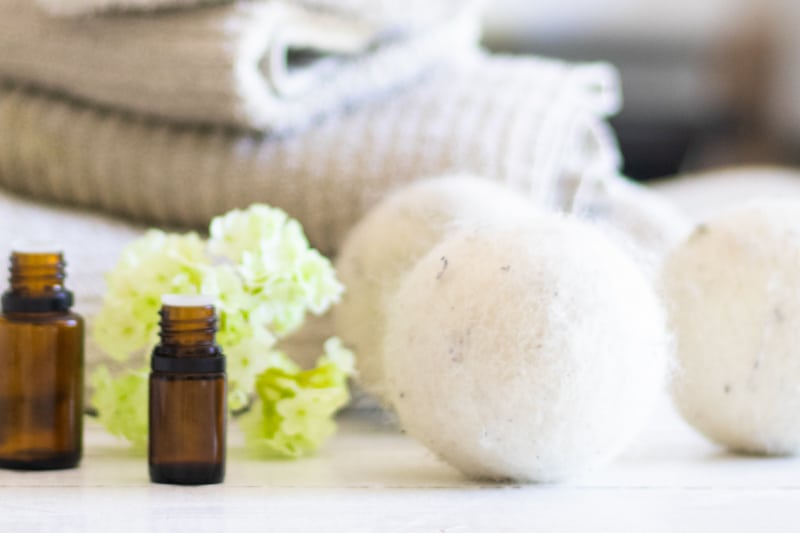 Wool dryer balls on white table with amber colored essential oil bottles next to them.