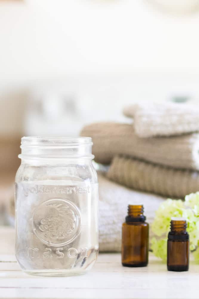 Homemade fabric softener in glass mason jar with clean towels behind it.