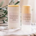 Two body butter sticks on white and black stripe towel.