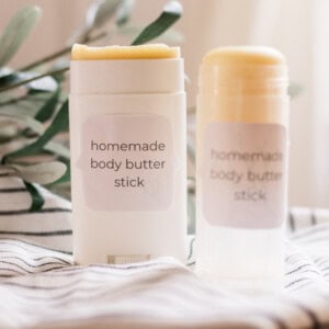 Two body butter sticks on white and black stripe towel.