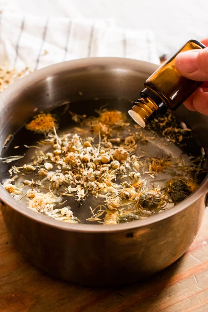 Women adding drops of essential oils to pot of water and dried herbs.