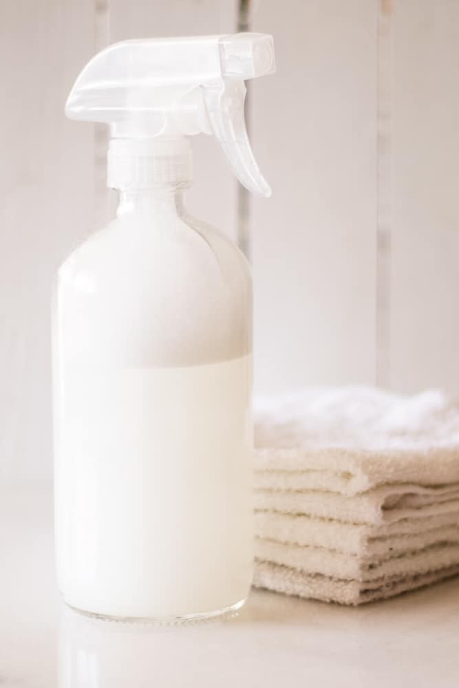 White glass spray bottle with white cloths next to it.