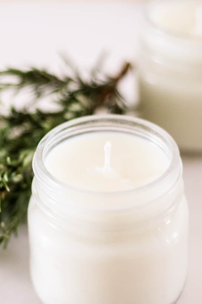 Rosemary mint soy candle in a small mason jar with rosemary sprig next to it. 