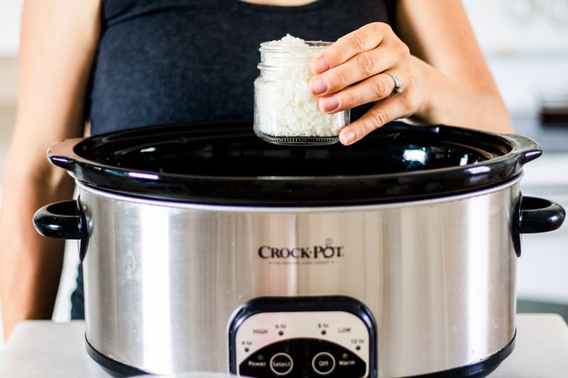 Women placing mason jar of wax into a crock pot. 