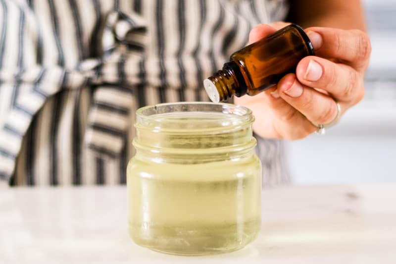 Women adding essential oils to melted wax in mason jar.