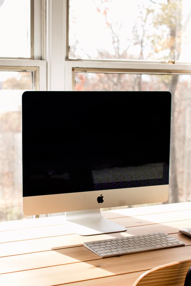 Mac desktop on desk in front of window.