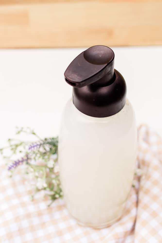 Homemade foaming hand soap in clear glass soap dispenser on white and grey checkered towel.