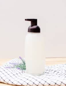 Organic foaming hand soap in a glass soap pump dispenser on countertop.