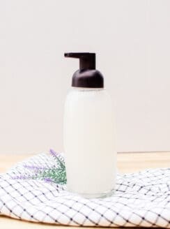 Organic foaming hand soap in a glass soap pump dispenser on countertop.
