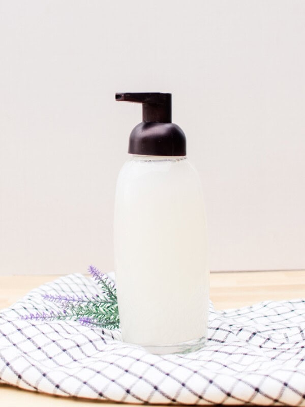 Organic foaming hand soap in a glass soap pump dispenser on countertop.