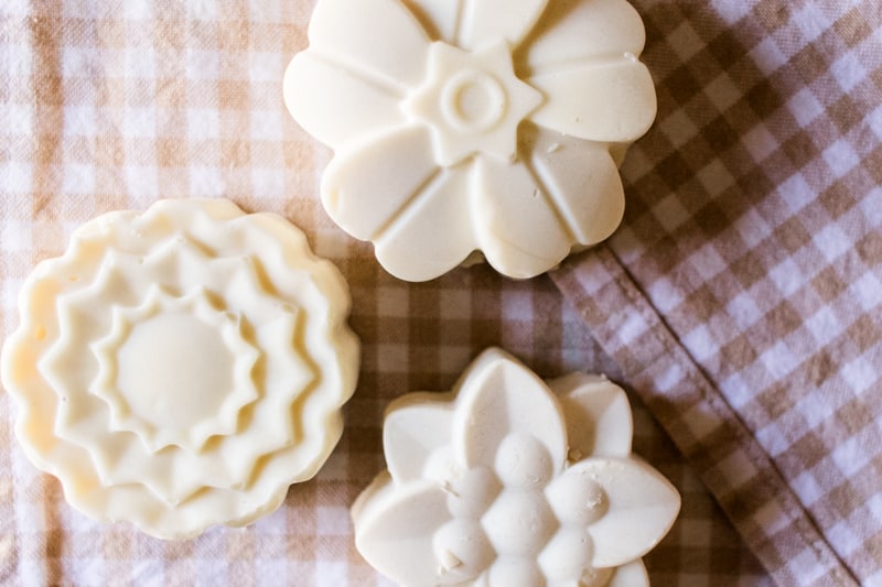 Three soap bars shaped like flowers on white and tan checked towel.