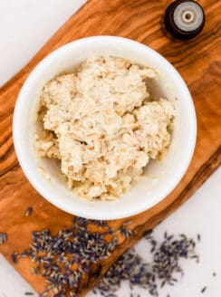 DIY hand mask in a small mixing bowl with lavender on a wooden tray on a white marble countertop.