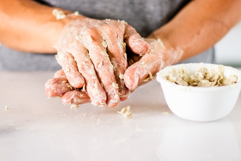 Bowl of oatmeal hand mask sitting next to hands covered lotion.