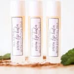 3 DIY lip balms in clear tubes with homemade labels on white marble.