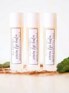 3 DIY lip balms in clear tubes with homemade labels on white marble.