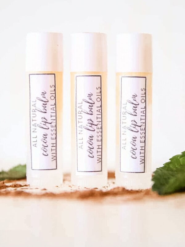 3 DIY lip balms in clear tubes with homemade labels on white marble.