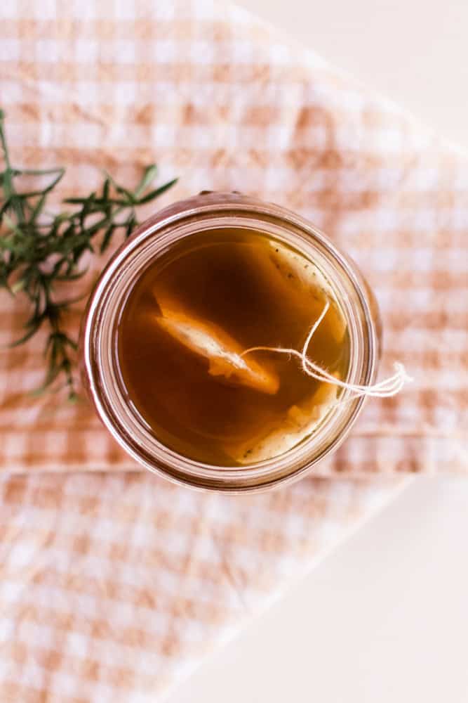 Green tea hair rinse in mason jar sitting on white table on a tan and white checkered towel.