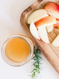 DIY clarifying shampoo with apple cider vinegar in a small glass jar with a cutting board of sliced apples.