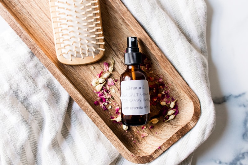 DIY sea salt spray on wooded tray with a comb and rose petals.