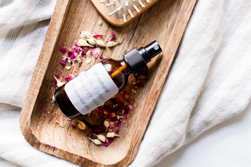 Salt spray for curly hair on wooden tray with sea salt and rose petals.