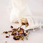 Herbal bath tea spilling out of a muslim tea bag on a white marble vanity.