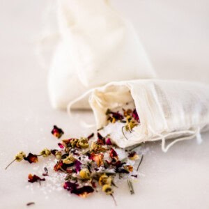 Herbal bath tea spilling out of a muslim tea bag on a white marble vanity.