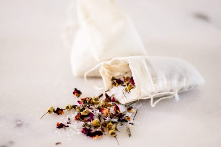 Herbal bath tea spilling out of a muslim tea bag on a white marble vanity.