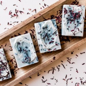 Loofah soap bars on a wooden soap tray garnished with hibiscus flowers.