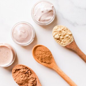 Top 3 best natural concealer recipes in small glass containers with the different color pigments in wooden spoons.