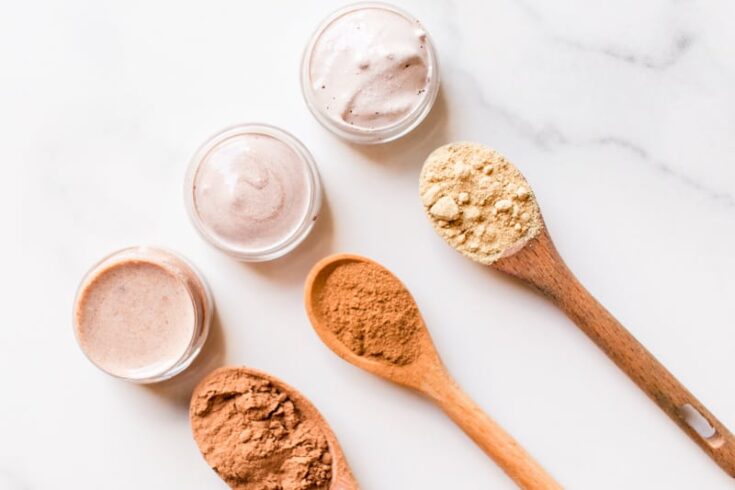 Top 3 best natural concealer recipes in small glass containers with the different color pigments in wooden spoons.