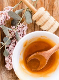 Homemade honey face mask being stirred in with a wooden spoon on a wooden table.